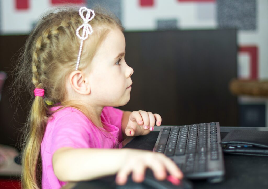 Side view of young girl looking at a computer screen, her hand on the mouse.