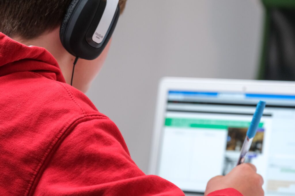 Over the shoulder view of a boy working on a laptop with headphones on.