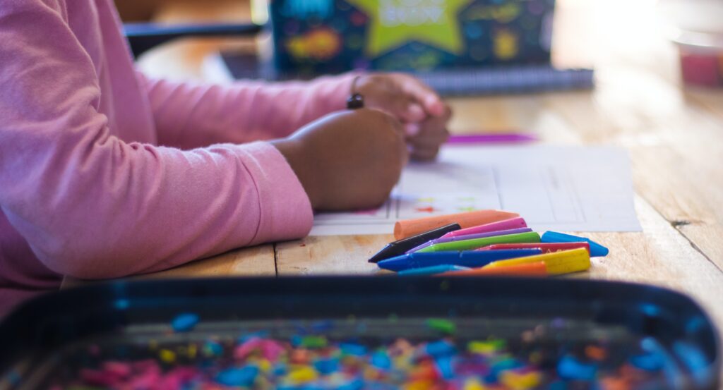 Young girl's hands working with crayons on a worksheet.