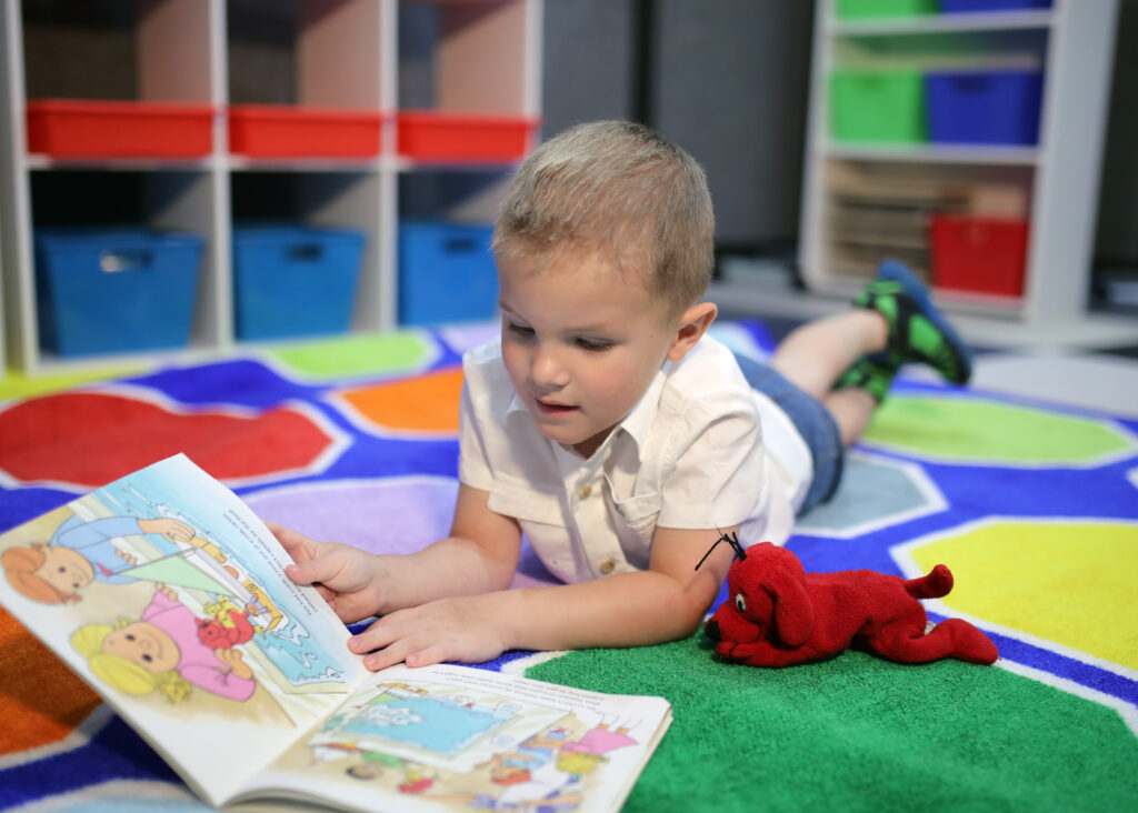 Boy laying on carpet at CLEAR reading Clifford.